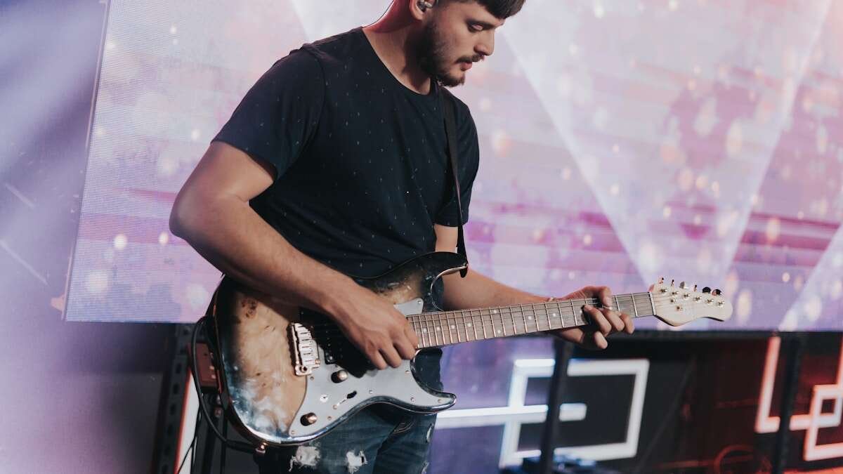 Glazbenik svira električnu gitaru na koncertu, naglašavajući energiju i dinamiku modernog rock nastupa.