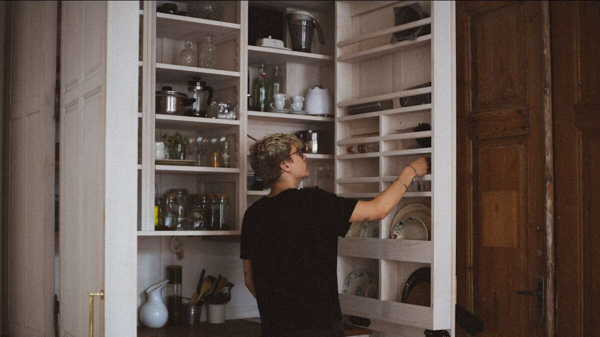 Osoba popravlja labava vrata kuhinjskog ormarića pomoću alata, fokus na rukama i šarkama.