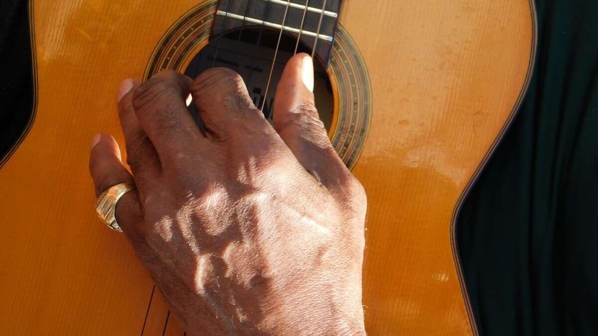 Blizak prikaz ruke koja drži vrat gitare i pritiska žice, fokusirajući se na tehniku sviranja.