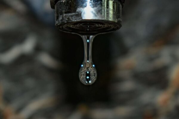 Blizak prikaz slavine iz koje kapa voda, s kapljicama koje se jasno vide na slavini.