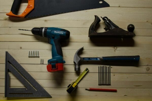 Prikaz osnovnih alata za popravak zida, uključujući gletericu, brusni papir i glet masu, na radnoj površini.