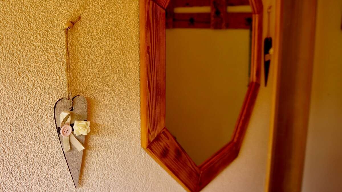 Ruke koje pažljivo postavljaju ogledalo na zid koristeći nosače i nivo