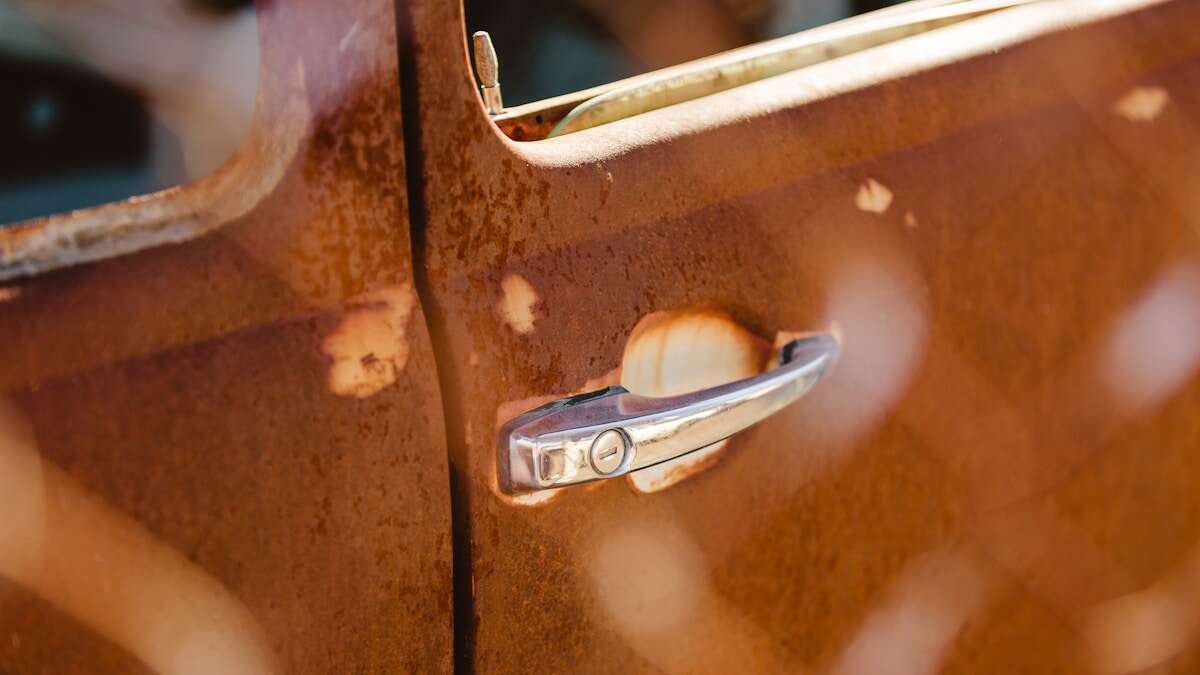 Makro prikaz zahrđale šarke na vratima, naglašavajući potrebu za čišćenjem i održavanjem.