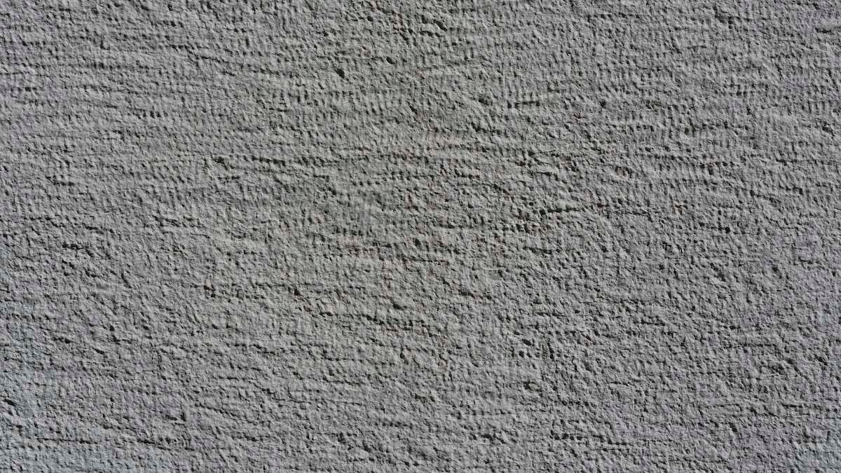 Ruka koja brusi popravljenu površinu zida brusnim papirom, pripremajući je za bojenje.