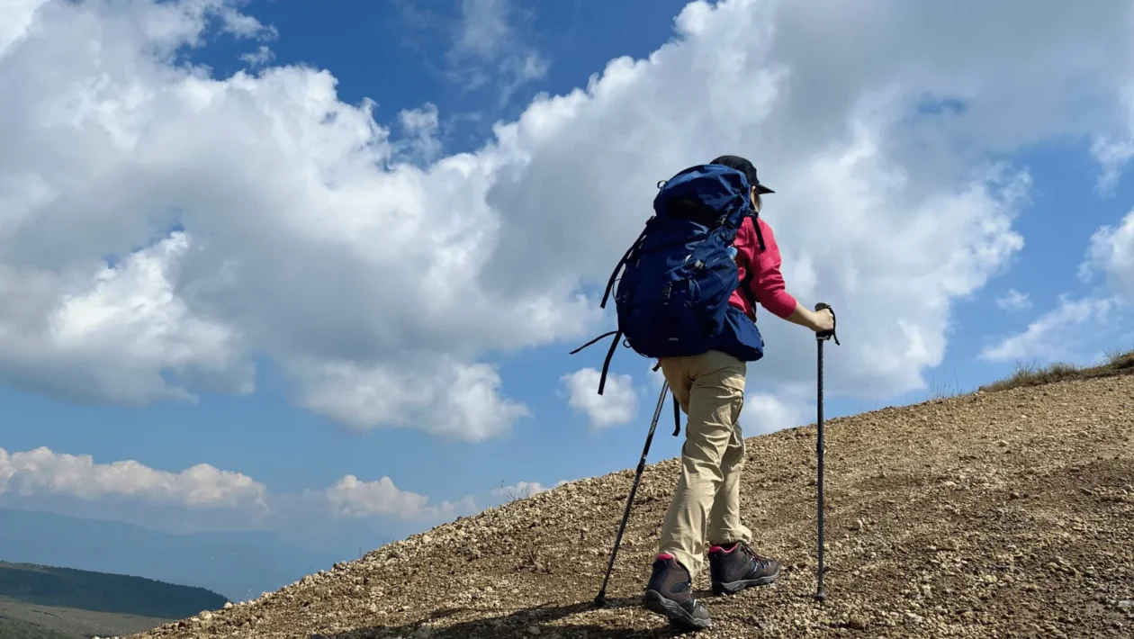 Planinar s ruksakom i štapovima na kamenitom usponu pod plavim nebom na Velebitu