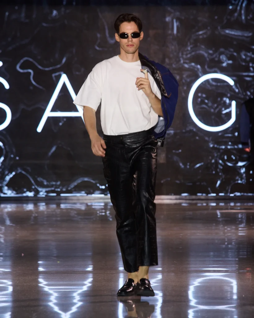 ŠARGI Denim muška kombinacija s bijelom majicom i crnim kožnim hlačama uz ležerni stav s jaknom preko ramena.