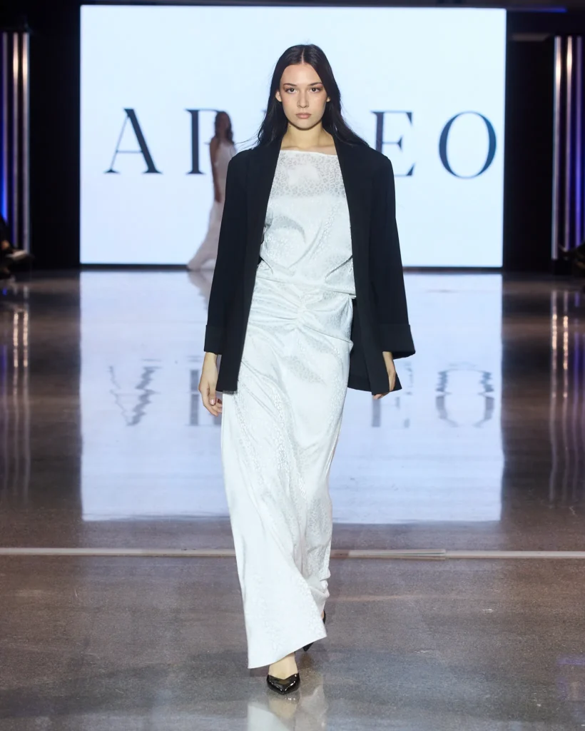 Model u dugoj bijeloj drapiranoj haljini kombiniranoj s crnim sakoom na Arileo pisti u Zadru.