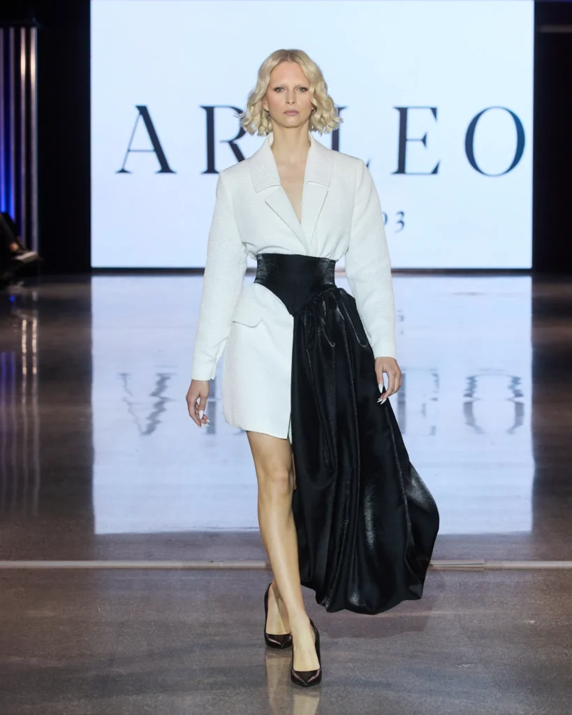 Model u bijelom sakou s naglašenim crnim voluminoznim detaljem i asimetričnom siluetom.