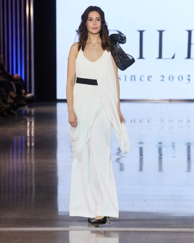 Model nosi bijeli voluminozni top s crnim asimetričnim detaljem i čipkastim hlačama iz Arileo kolekcije.