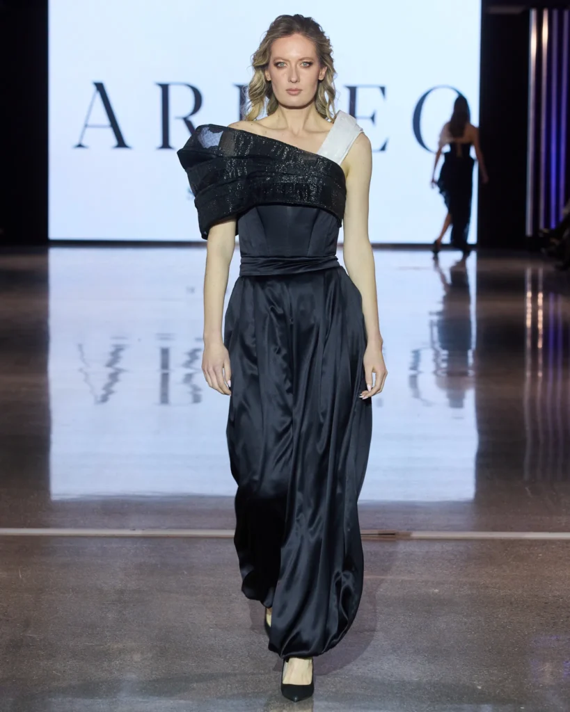 Model u elegantnoj crnoj svilenoj haljini s naglašenim ramenim volumenom tijekom modne revije Arileo.