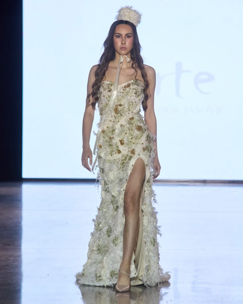 Bijela večernja haljina s visokim prorezom i bogatim floralnim aplikacijama.