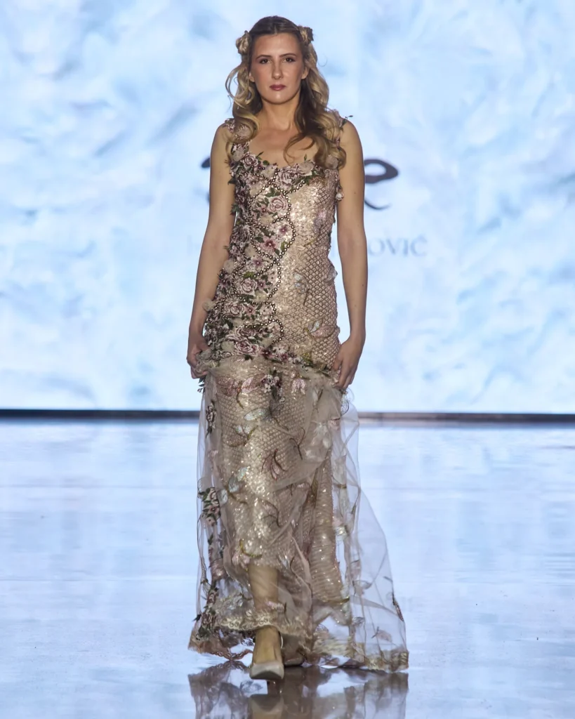 Metallic roza večernja haljina s prozirnim slojevima i floralnim aplikacijama.