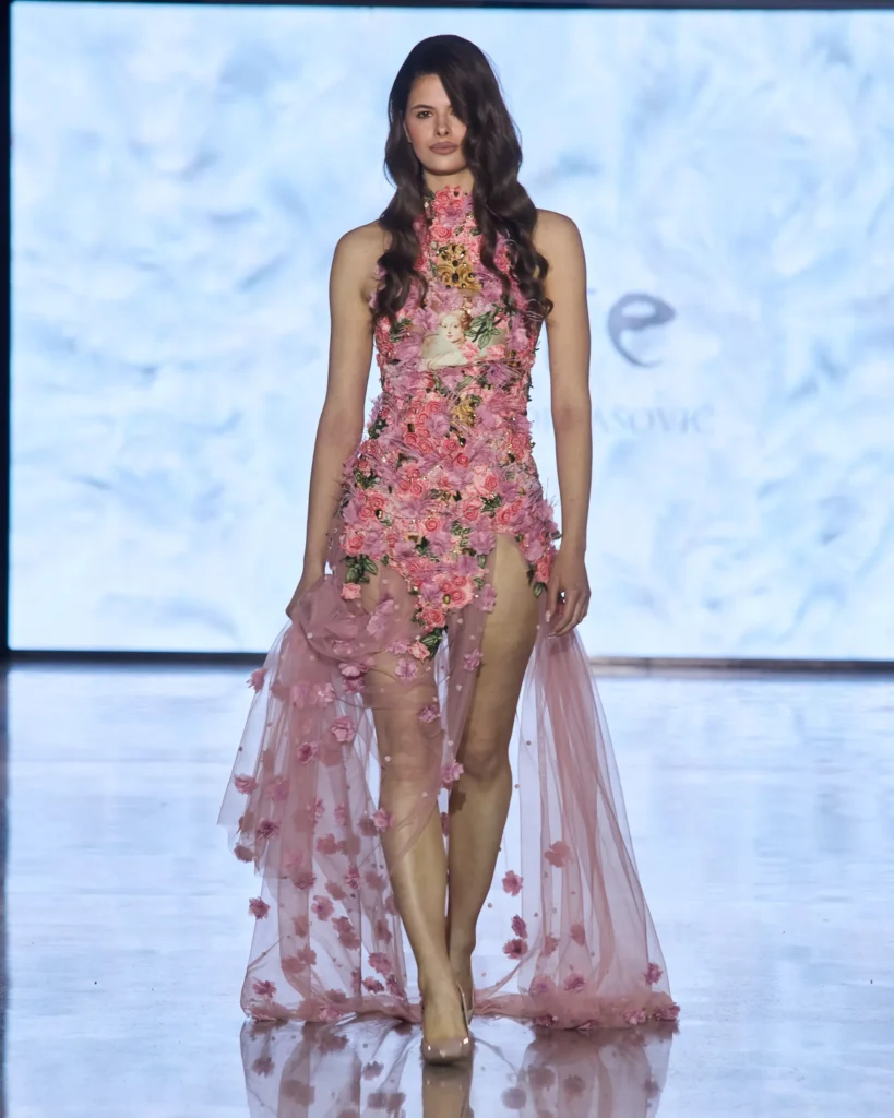 Asimetrična roza haljina prekrivena cvjetnim aplikacijama i laganim lepršavim slojevima.