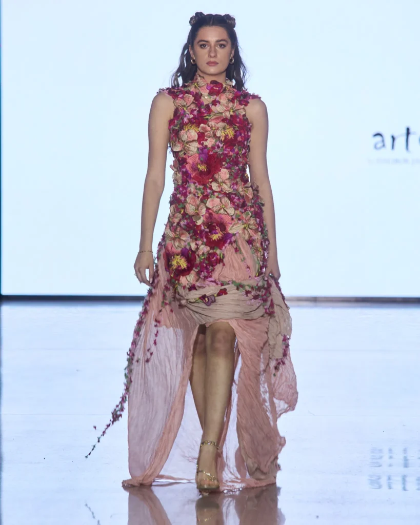 Roza haljina s produženim lepršavim donjim dijelom i trodimenzionalnim cvjetnim detaljima.