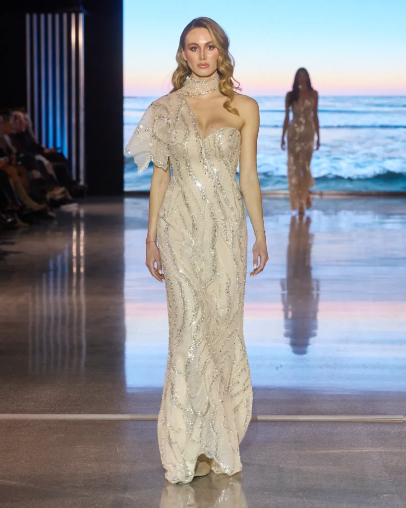 Krem večernja haljina s asimetričnim rukavom i sjajnim izvezenim uzorcima.