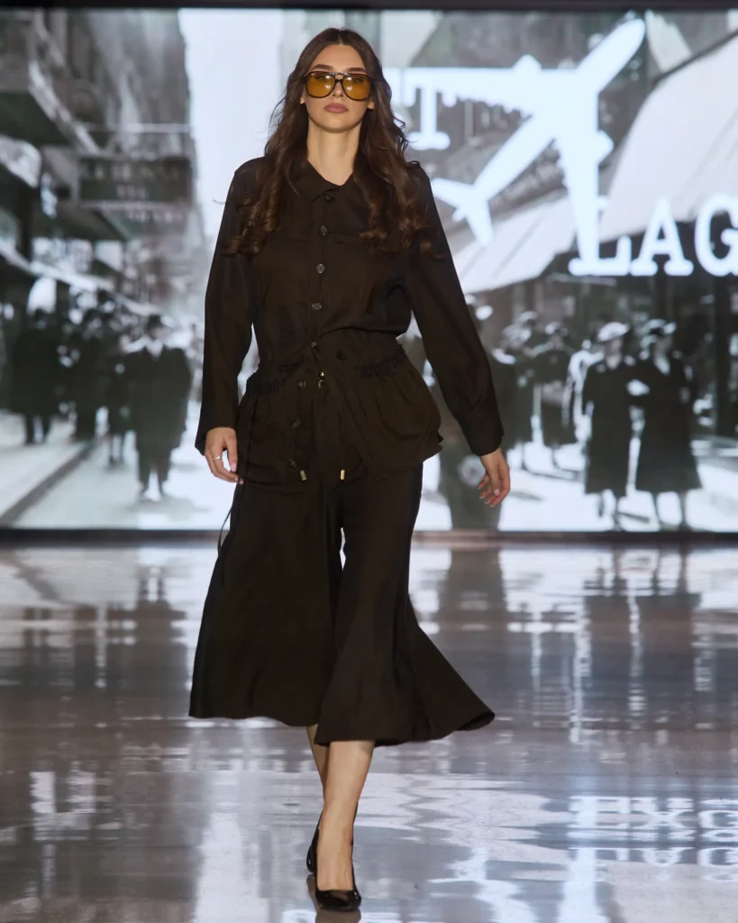 Crni set sa širokim hlačama i košuljom u utility stilu, upotpunjen žutim naočalama.