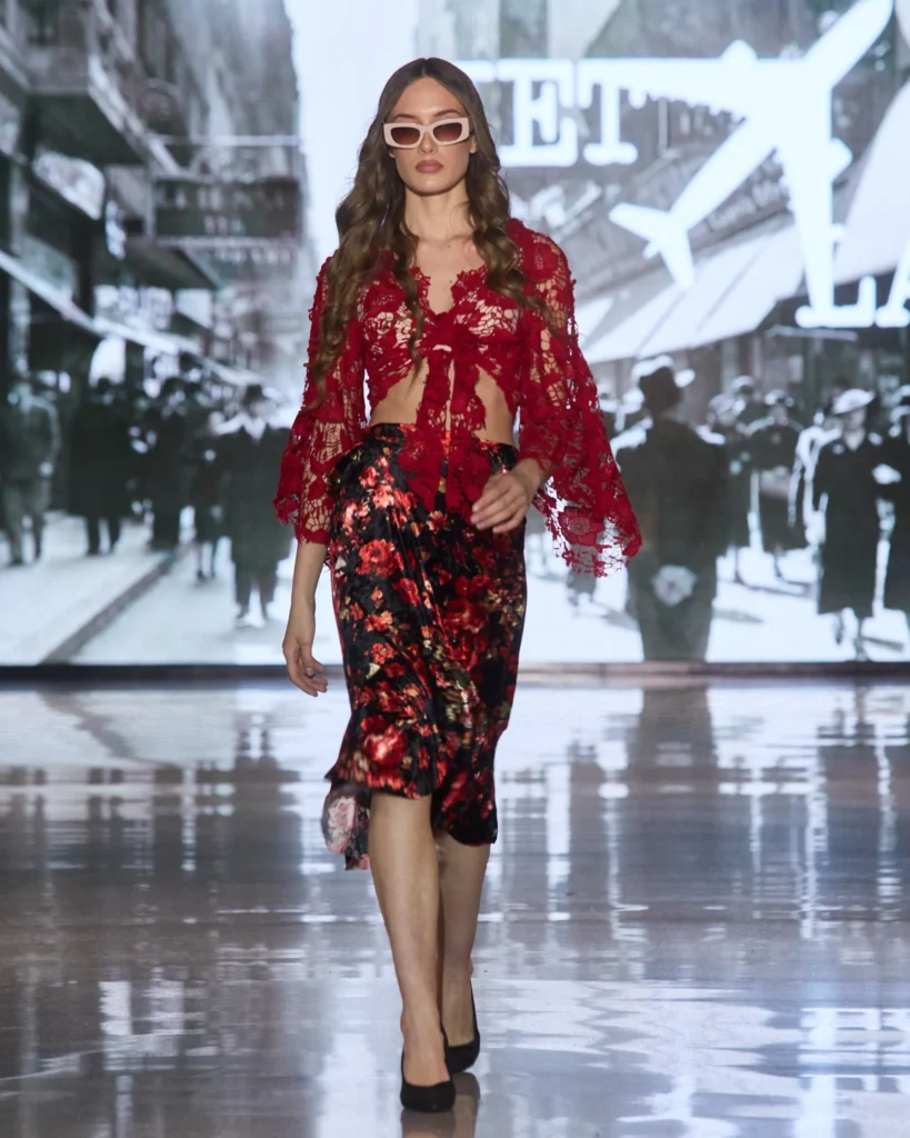 Crvena čipkana bluza s vezanim prednjim dijelom u kombinaciji s crnom midi suknjom s cvjetnim uzorkom.