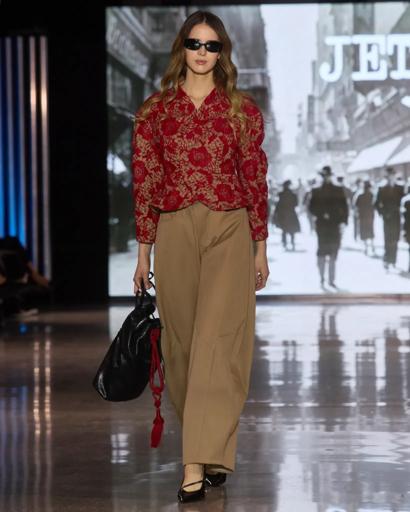 Crvena jakna s cvjetnim uzorkom u kombinaciji s bež širokim hlačama i oversized torbom.