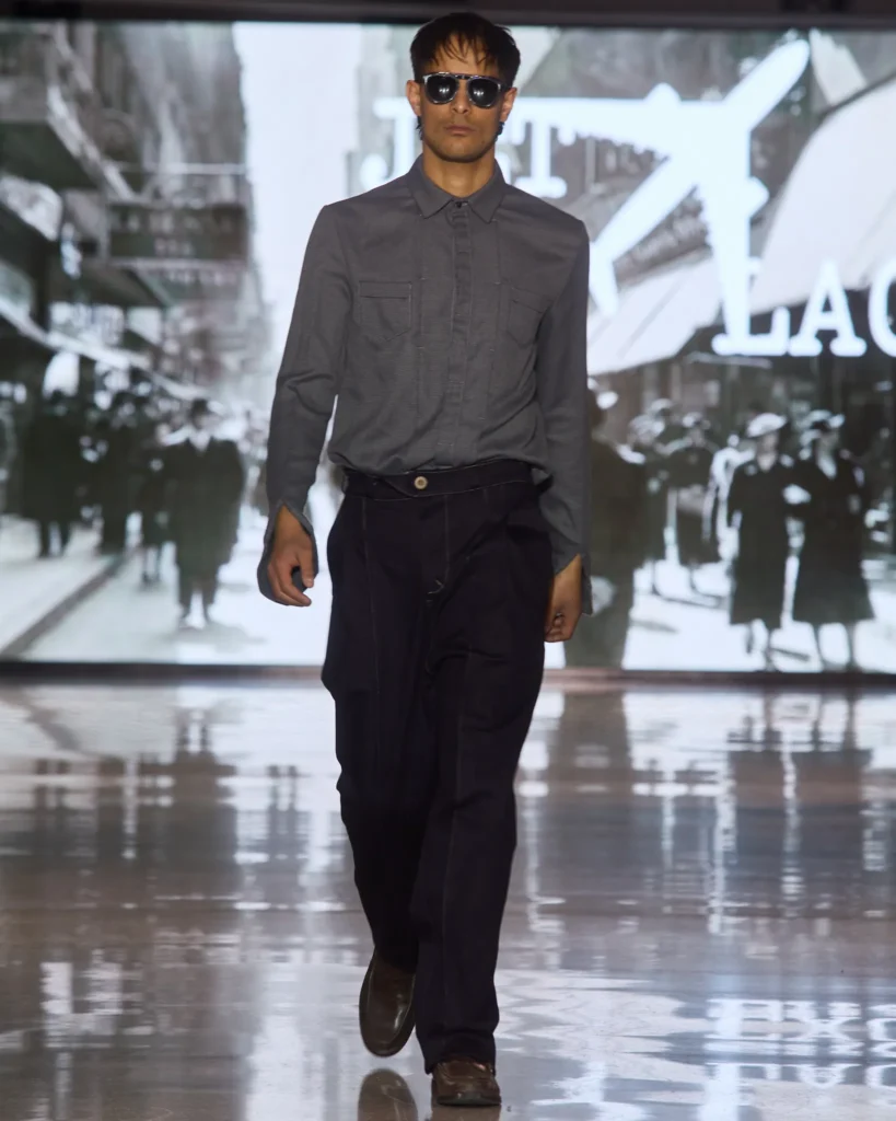 Tamna muška kombinacija s dugom sivom košuljom i crnim hlačama modernog kroja.