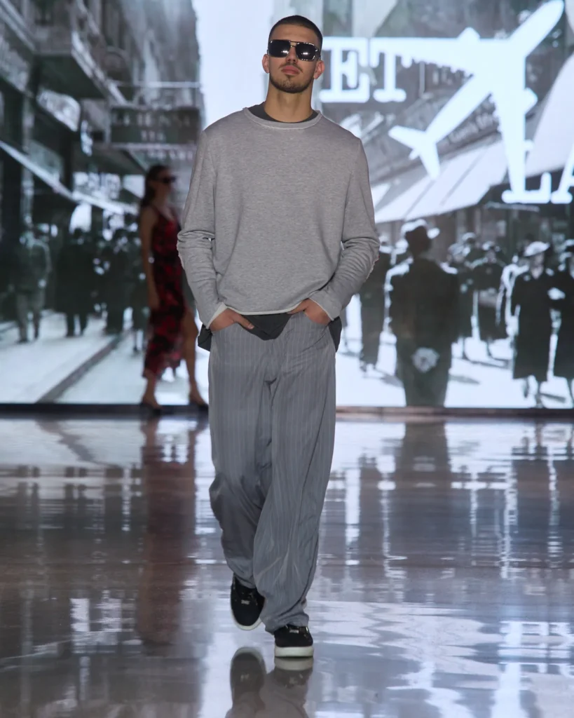 Muški sivi ležerni top u kombinaciji sa širokim prugastim hlačama i sportskim detaljima