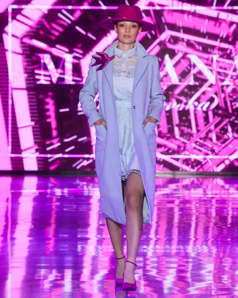 Lila kaput preko svijetle haljine, stiliziran s fuksija šeširom i brošem.