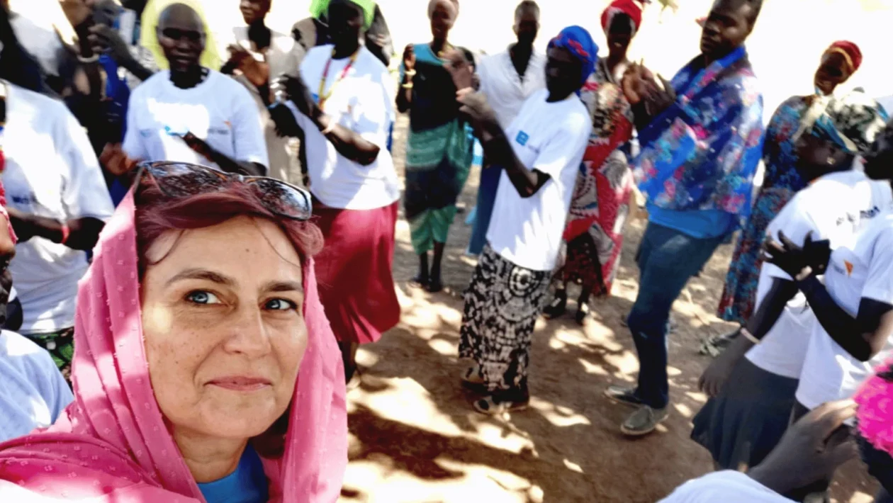 Žena s ružičastom maramom snima selfie s grupom ljudi koji plješću u pozadini