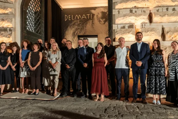 Grupna fotografija sudionika na noćnom otvaranju izložbe, poziranih ispred ulaza. Iza njih je osvijetljen ulaz s velikim zlatnim natpisom "DELMATI" i upečatljivim dizajnom koncentričnih krugova.