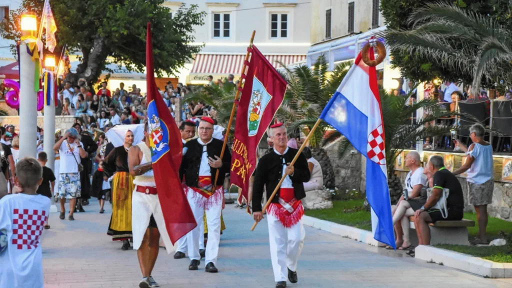 Povorka s hrvatskom zastavom i zastavama udruga. Karnevalska povorka i izvođenje paškog kola tijekom 67. Paškog ljetnog karnevala u gradu Pagu 2026.