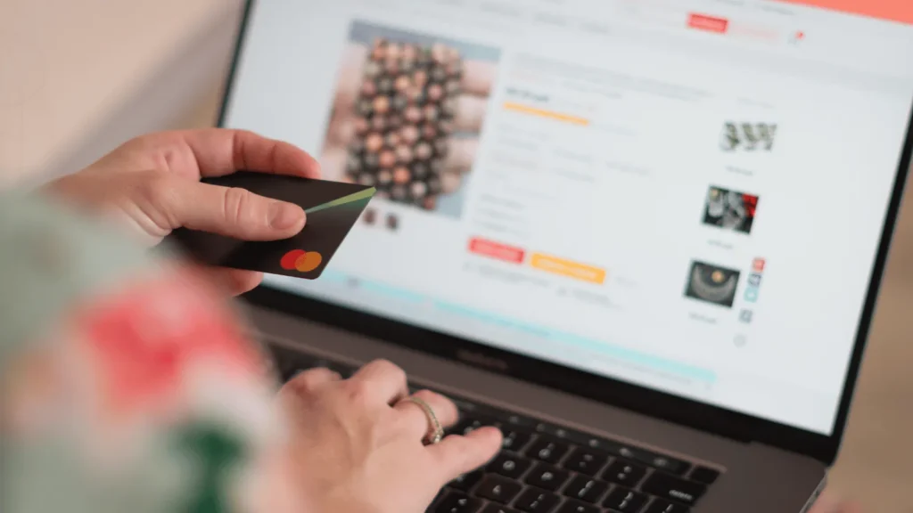 Osoba drži kreditnu karticu i unosi podatke na tipkovnici prijenosnog računala dok kupuje na internetu