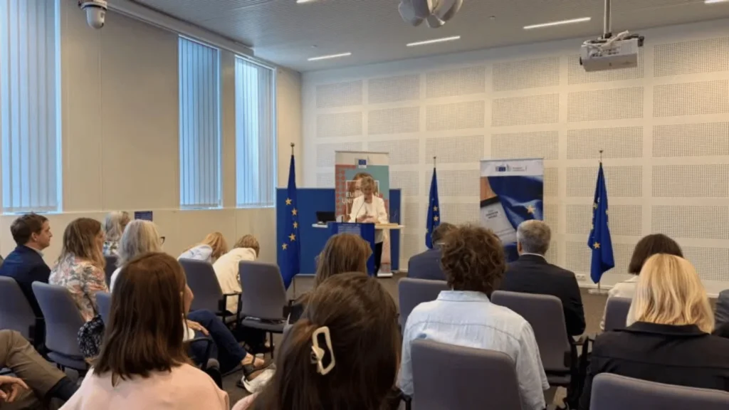 Žena drži govor pred publikom u sobi s europskim zastavama