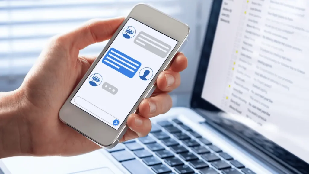 Chatbot su pametnom telefonu pored laptopa