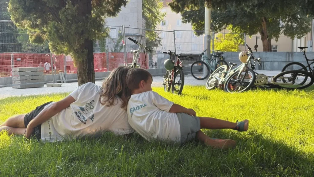 Dvoje ljudi leži na travi okruženi biciklima, dok je u pozadini gradilište
