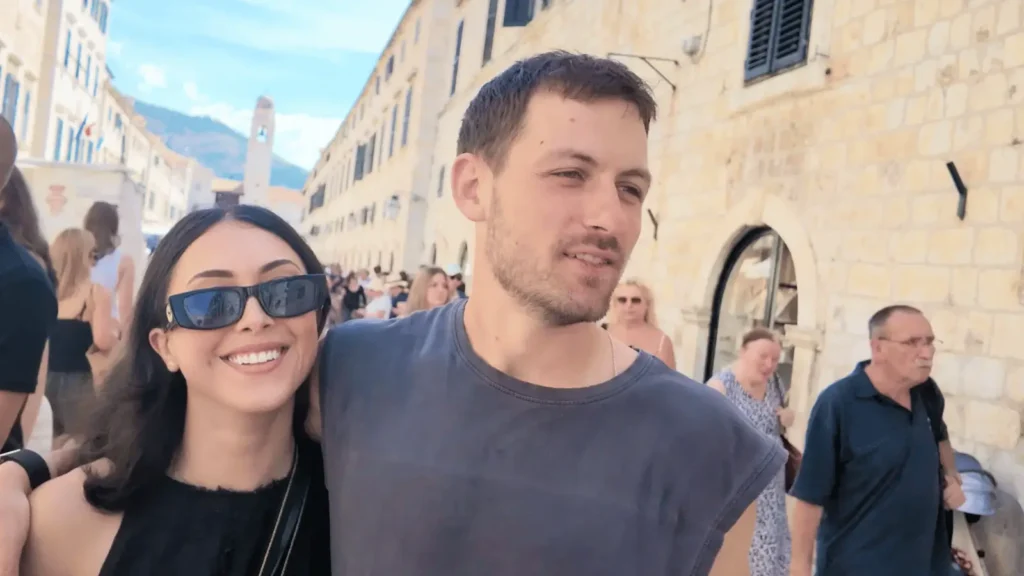 Mlada žena i muškarac zagrljeni hodaju ulicom s kamenim zgradama
