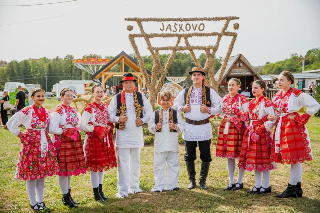 Skupina ljudi u narodnim nošnjama ispred natpisa "JAŠKOVO