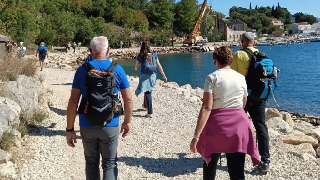 Ljudi šetaju kamenim putem uz obalu mora u sunčanom danu