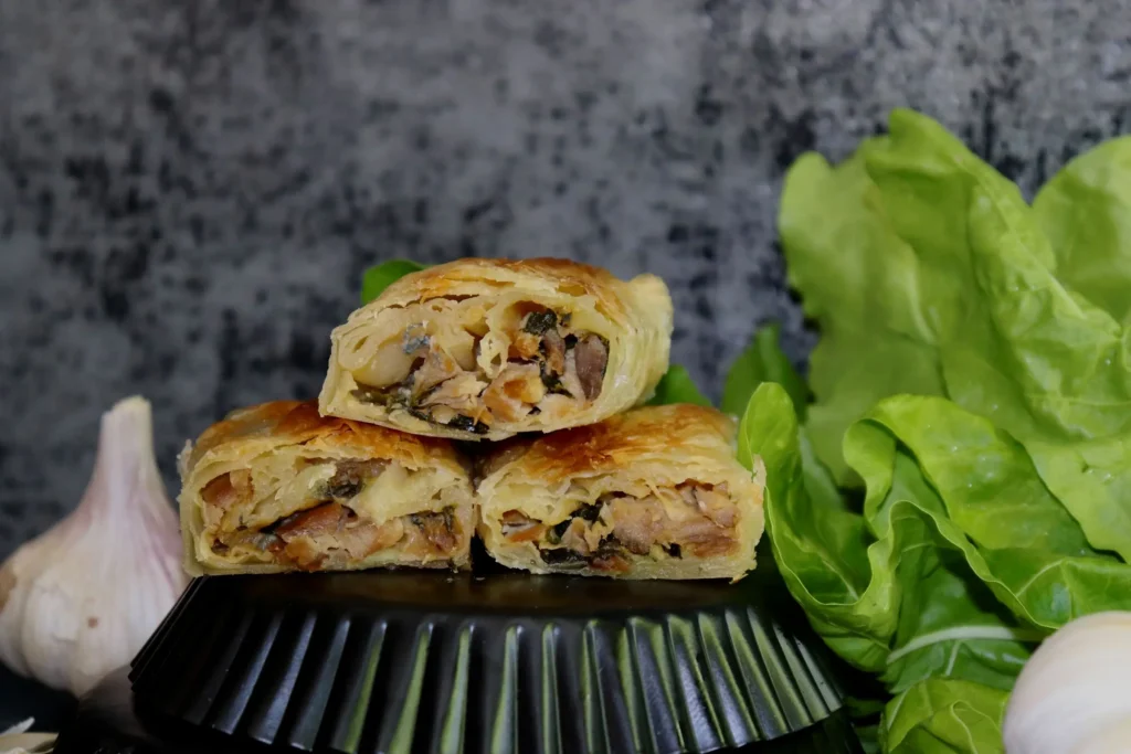 Tri pečene rolice s nadjevom od mesa i povrća, pored luka i listova zelene salate