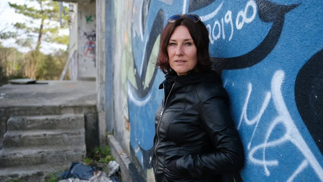 Žena u crnoj kožnoj jakni naslonjena na zid oslikan grafitima
