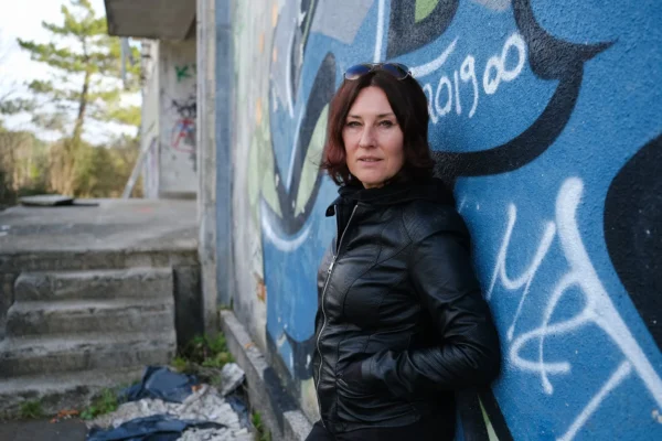 Žena u crnoj kožnoj jakni naslonjena na zid oslikan grafitima