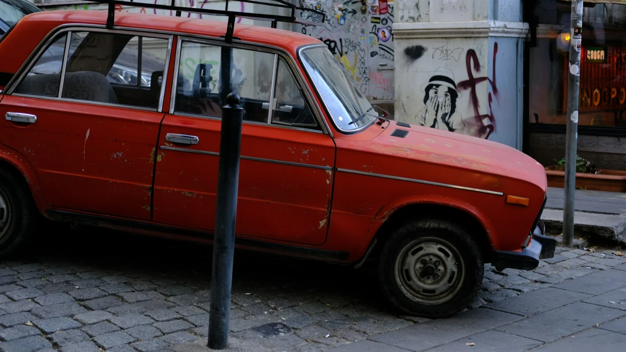 Crveni starinski automobil s krovnim nosačem parkiran na popločenoj ulici