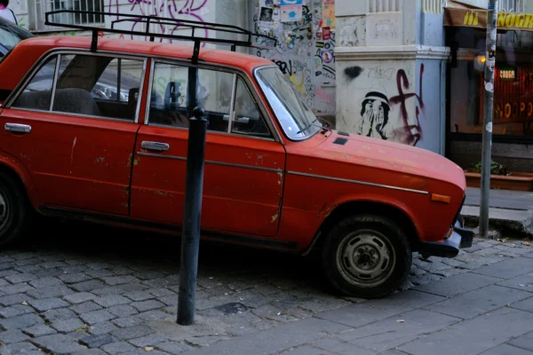 Crveni starinski automobil s krovnim nosačem parkiran na popločenoj ulici