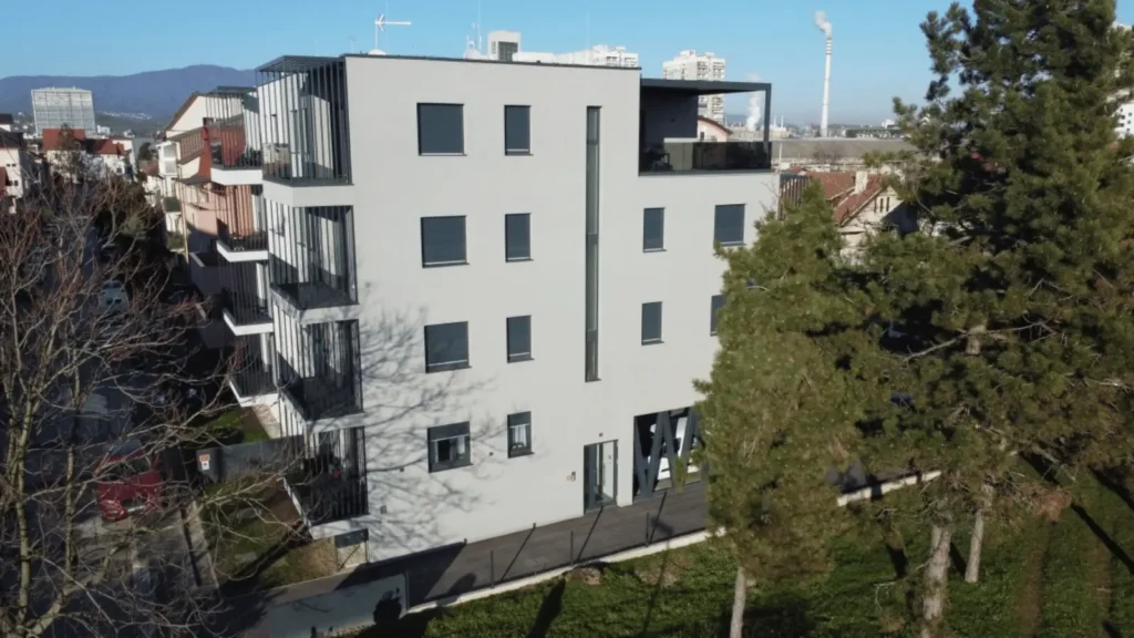 Moderna stambena zgrada s balkonima okružena drvećem i drugim zgradama