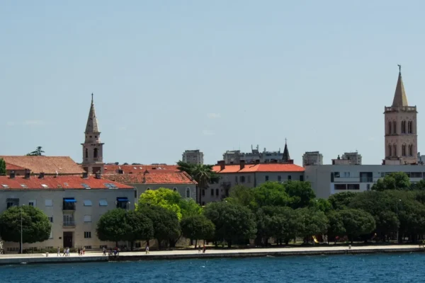 Pogled na gradsku obalu s crvenim krovovima, drvećem i tornjevima na sunčan dan