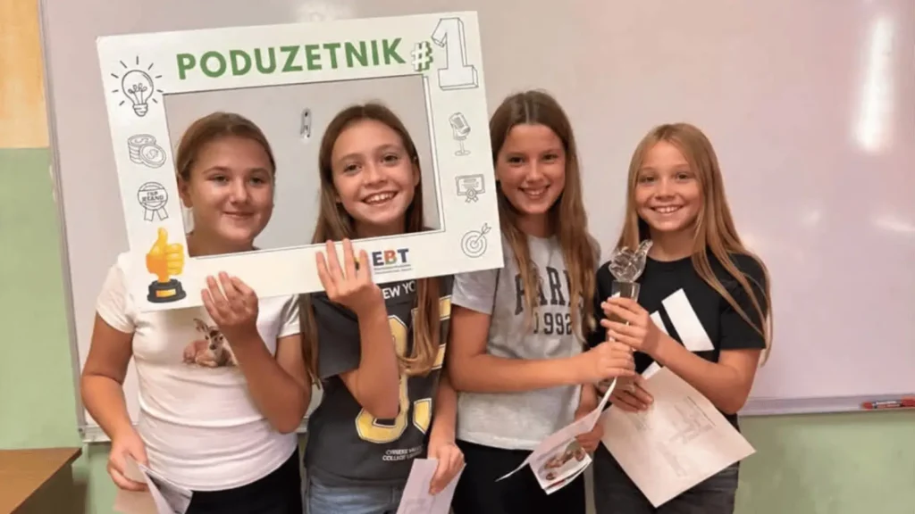 Četiri djevojčice drže okvir s natpisom "PODUZETNIK #1" i drže nagradu