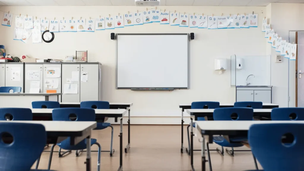 Prazna učionica s klupama, stolicama, bijelom pločom i abecedom obješenom na zidu